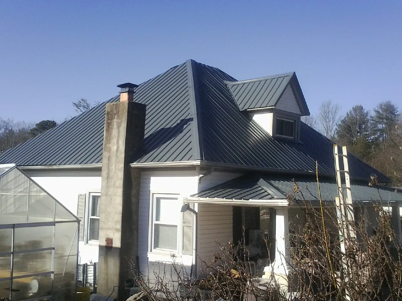 Dark blue standing seam metal roof on a white farmhouse with dormer — Slate & Tile Roof Repair by Roofing Brothers in Forest City
