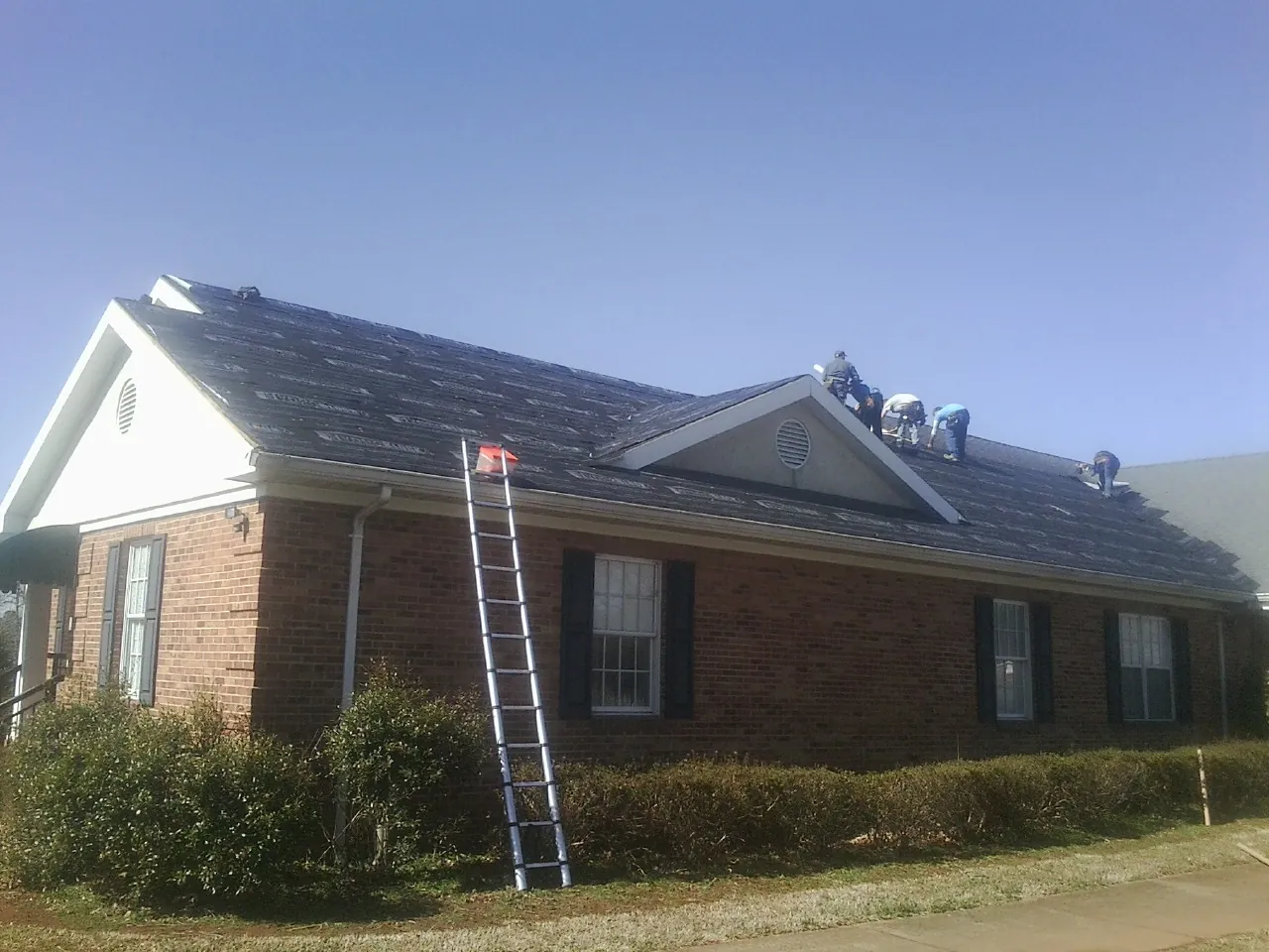 Crew tearing shingles off a brick ranch roof with a ladder set — Emergency Roof Repair work by our crew in Forest City