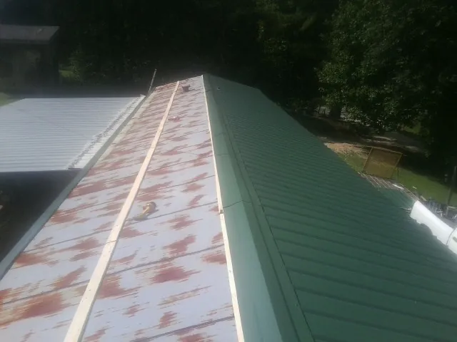 Old rusted panels beside newly installed green metal roofing — Wind Damage Roof Repair by Roofing Brothers in Forest City