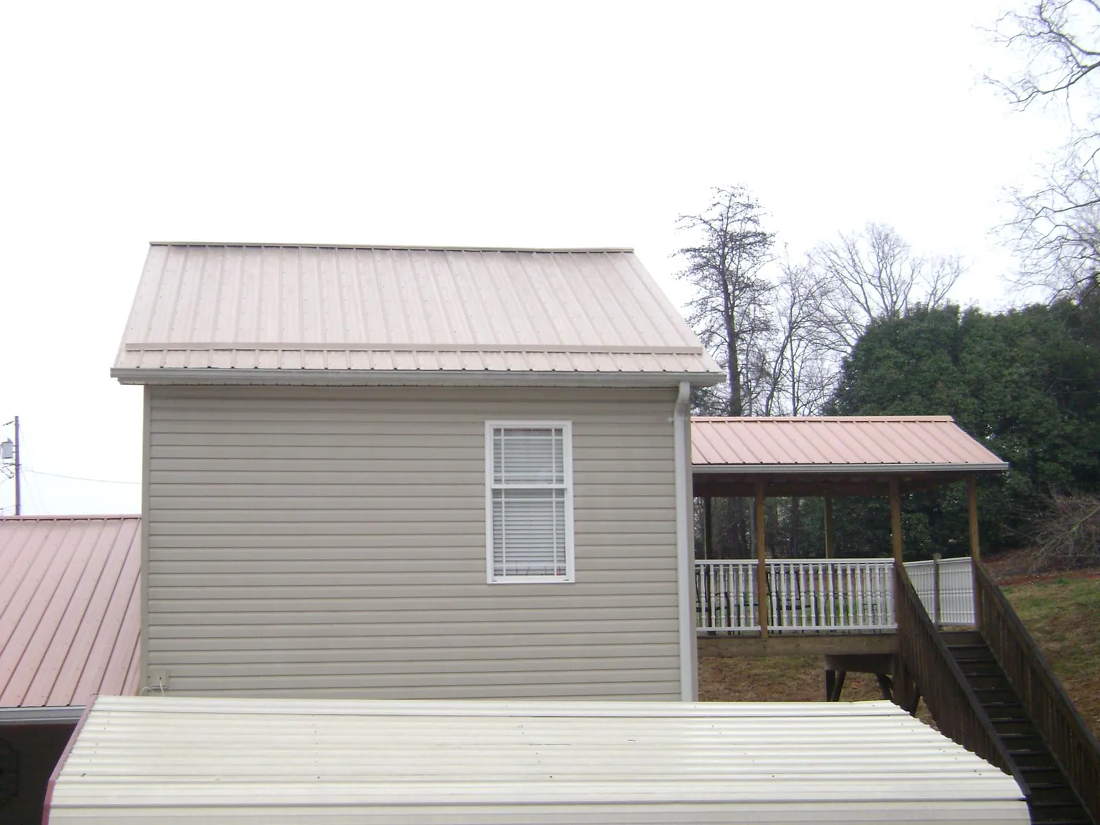 Tan metal roofs on a two story addition and attached porch, from a Roof Replacement job in Forest City
